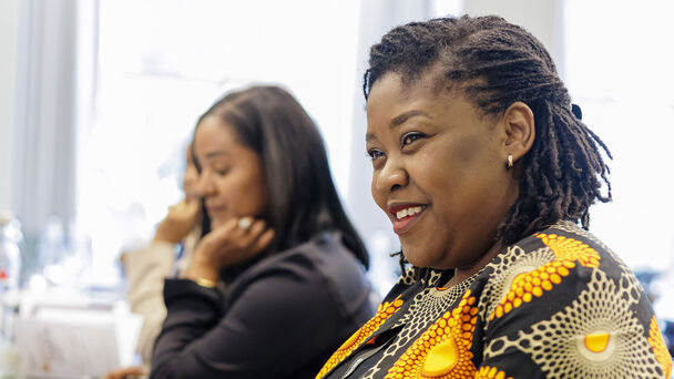 mehrere mutmaßlich afrikanische Frauen sitzen in einer Reihe, die Frau im Vordergrund lächelt