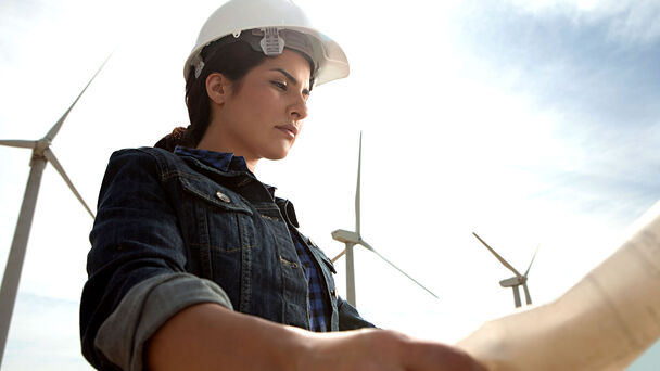 junge Frau bei einer Windfarm mit Plänen in der Hand