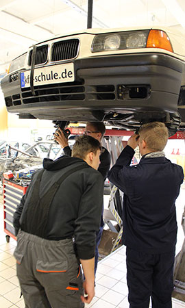 Szene einer Ausbildung, junge Männer arbeiten an Unterboden eines Autos