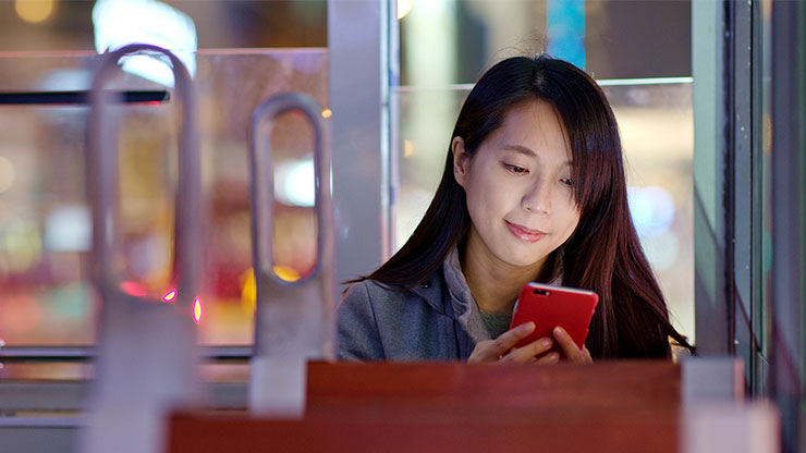 junge Chinesin schaut auf Smartphone in einer Bahn