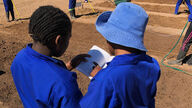 two Namibian trainees in work clothes read a brochure together