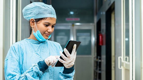 Woman in surgical gown taps on a tablet